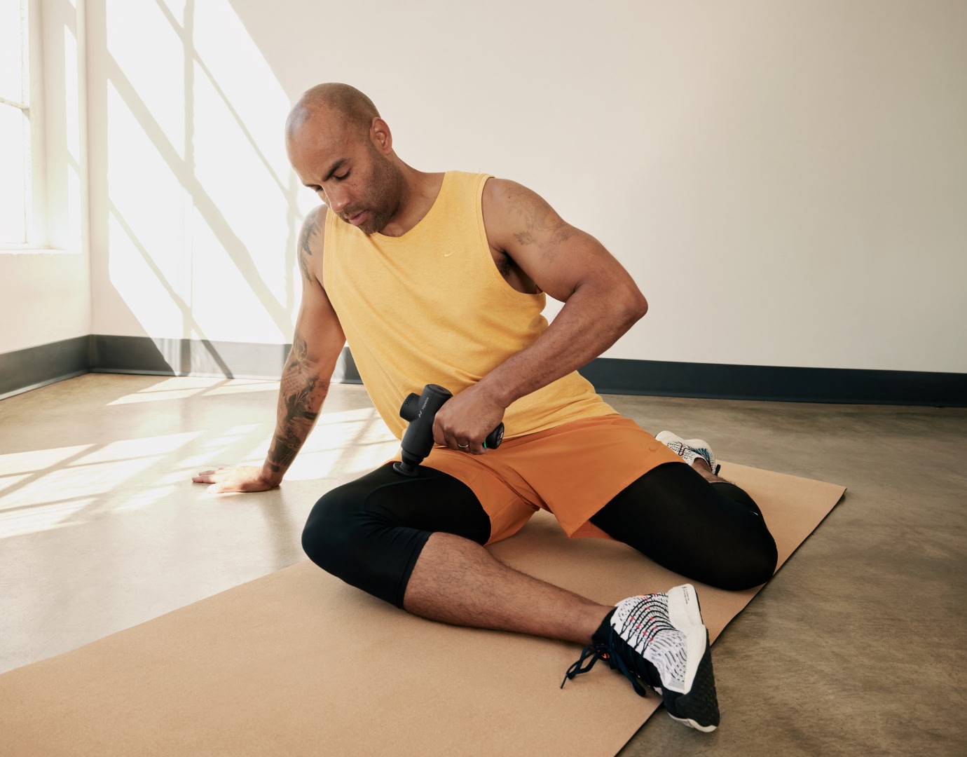 Man seated on yoga mat using Hypervolt massage gun on right upper thigh.
