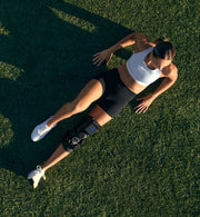 person laying on a grassy field with her leg outstretched wearing a hyperice x 2 knee device.