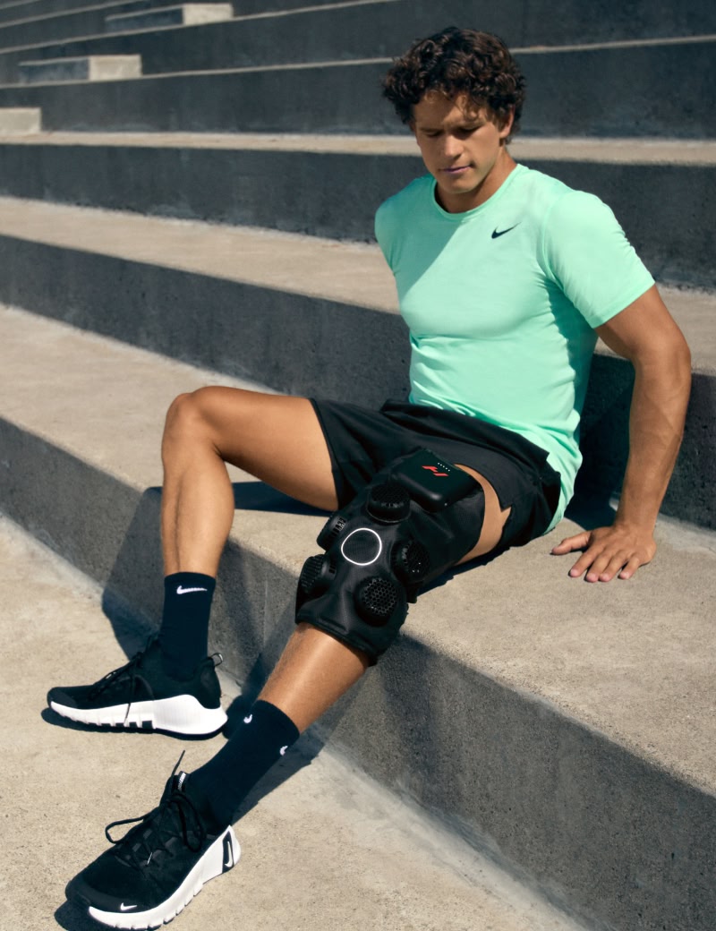 Homme assis sur des marches portant un t-shirt vert Nike et un dispositif Hyperice x 2 pour les genoux.