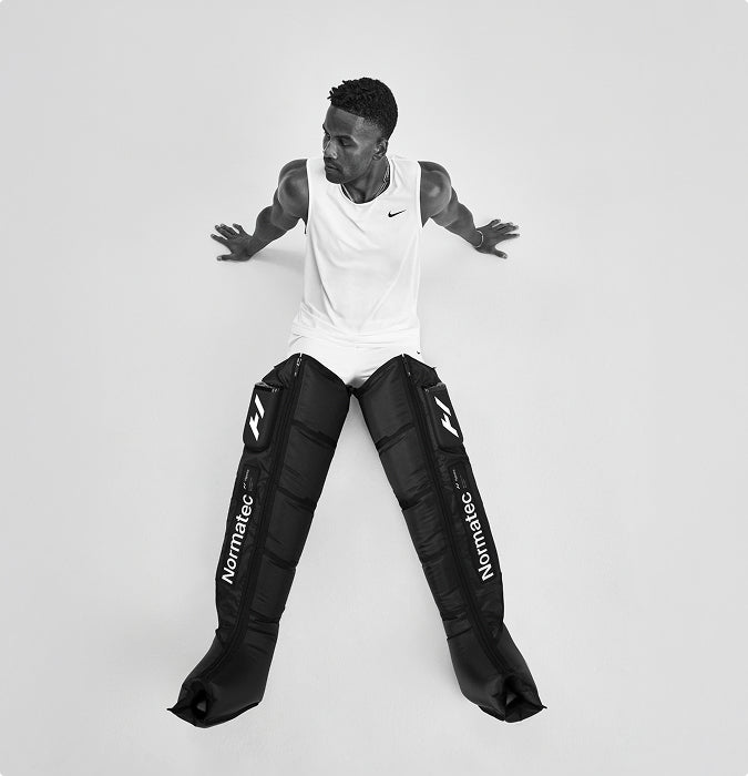 Person sitting on ground wearing Normatec elite legs on a white background
