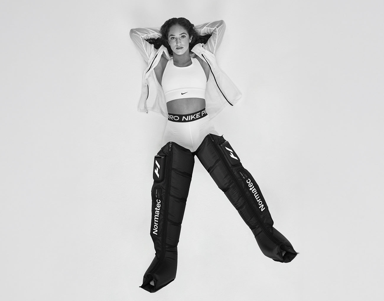 Person laying down looking up, wearing a Nike outfit with Normatec Elite Legs on, on a white background