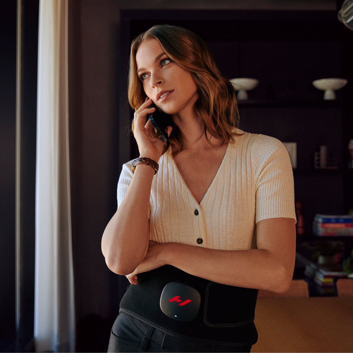 Woman talking on a phone with a Venom 2 Back device on her lower back in a dimly lit room.