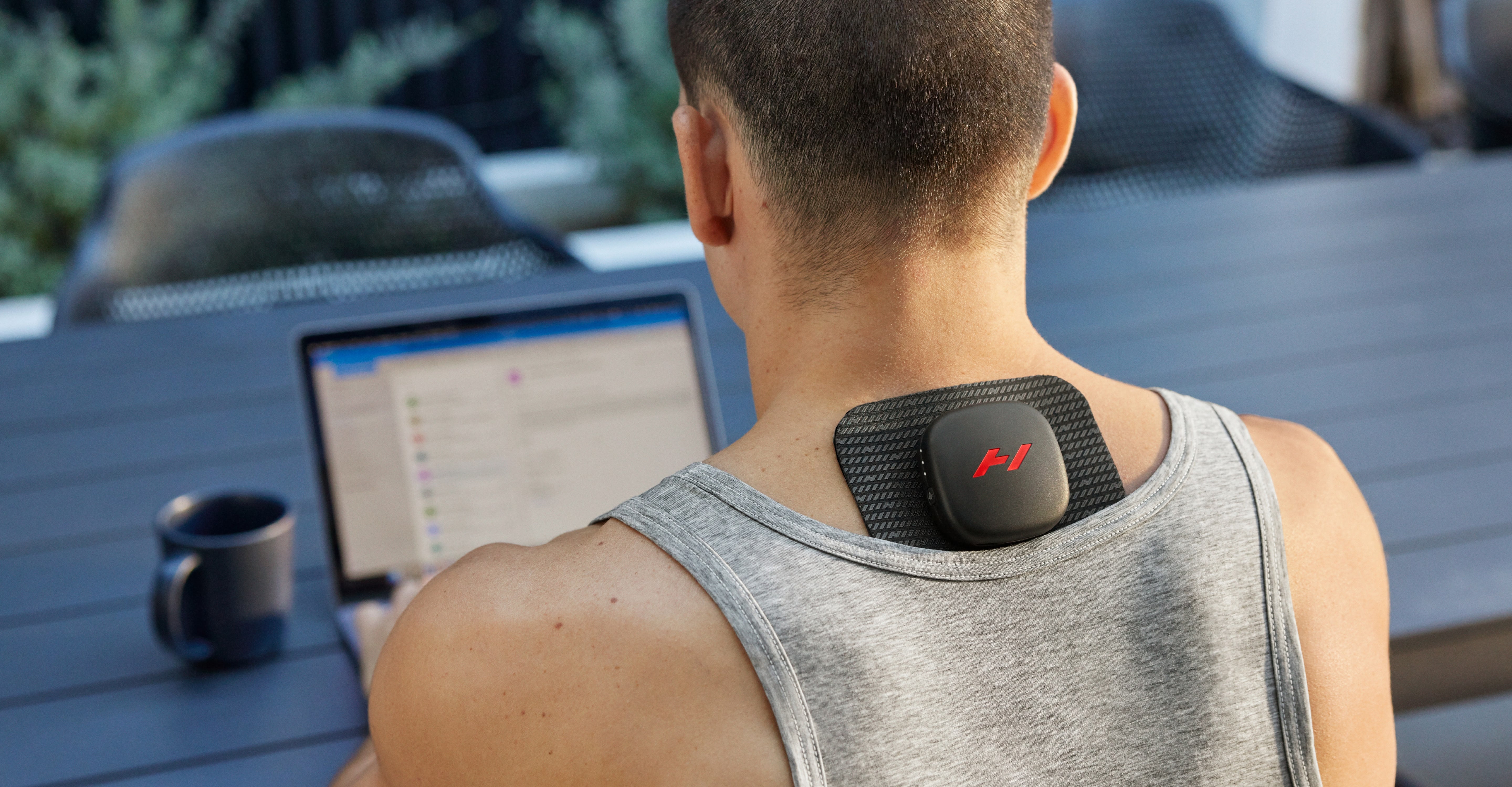 Person using a laptop sitting at a table outdoors, with a Venom Go on their upper back