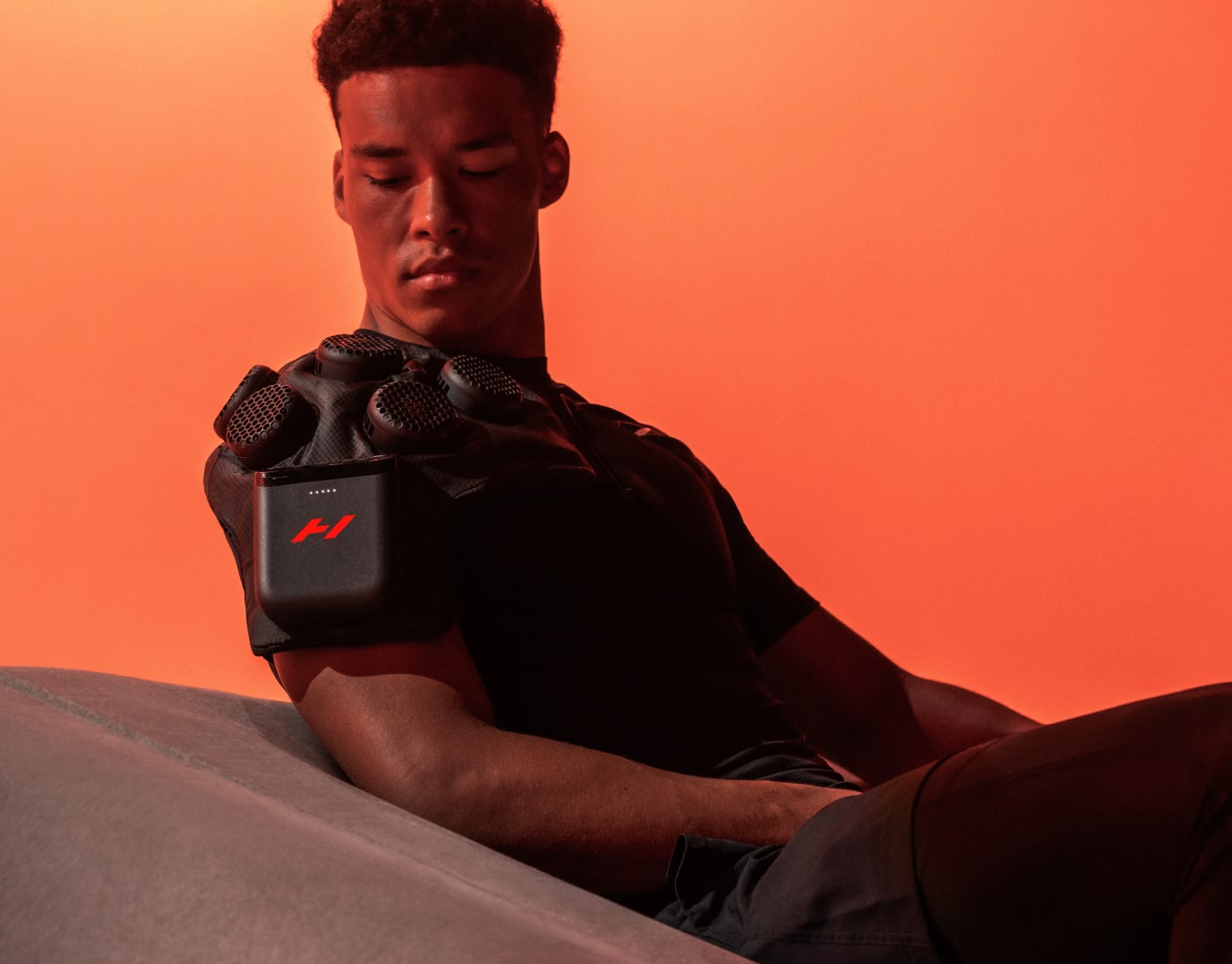 Man seated on couch wearing hyperice x 2 contrast therapy device on his shoulder.