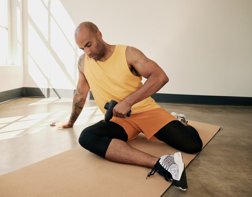 Man seated on yoga mat using Hypervolt massage gun on right upper thigh.