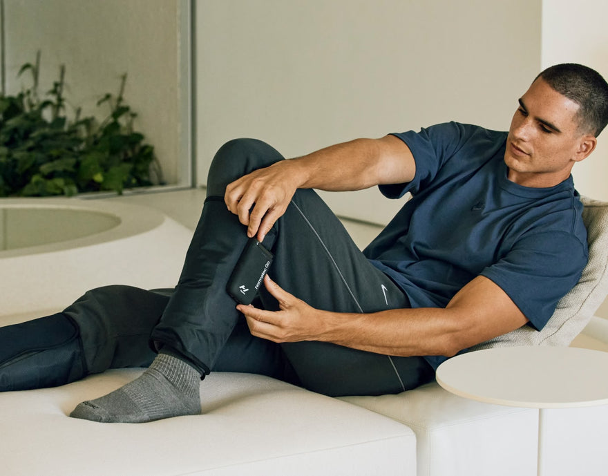 Man sitting on couch with Normatec go compression sleeves on his legs. 