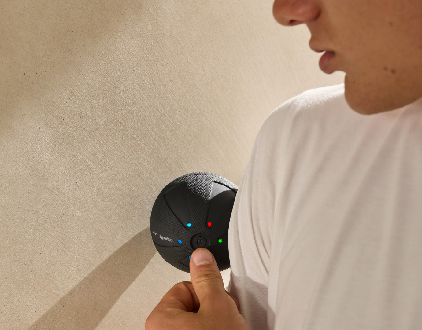 Man using Hypersphere Go massage ball roller on shoulder up against a wall.