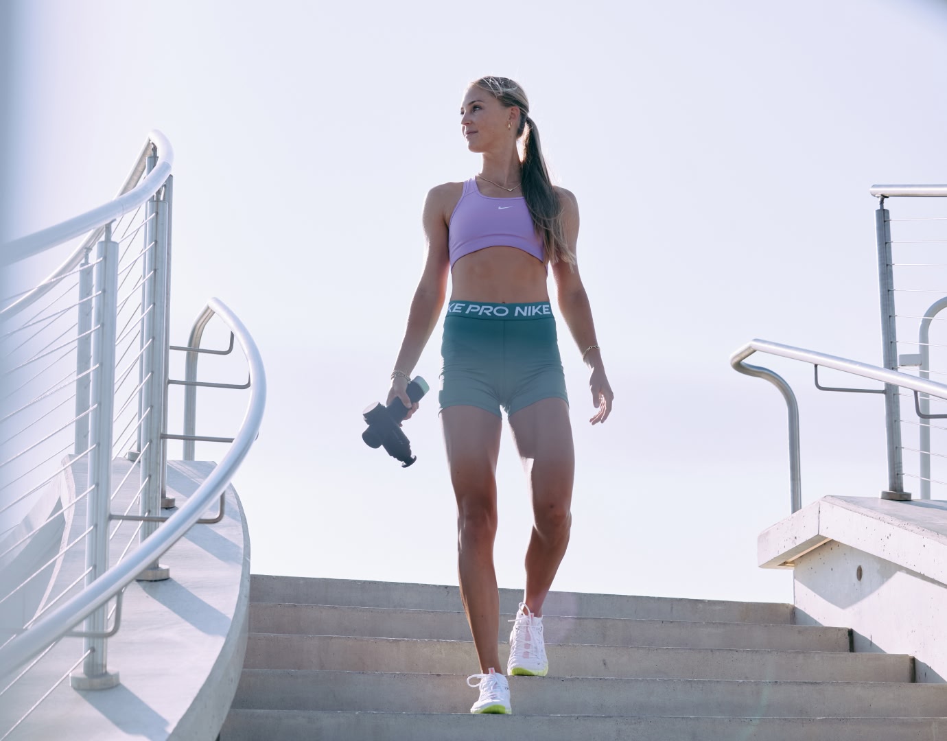 Woman outdoors walking down stairs with hypervolt massage gun in hand.