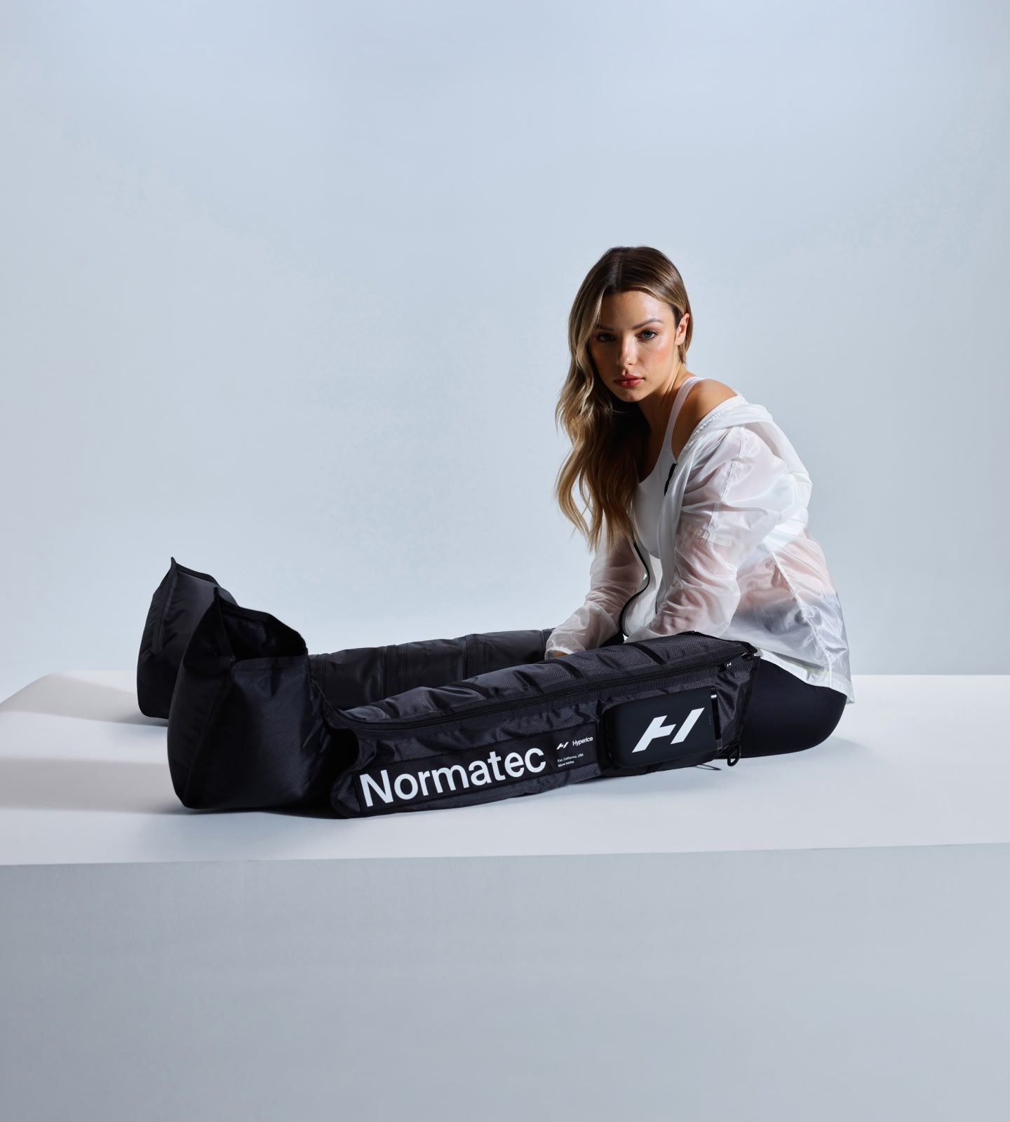 Woman using a Normatec Elite Legs compression device on a white background