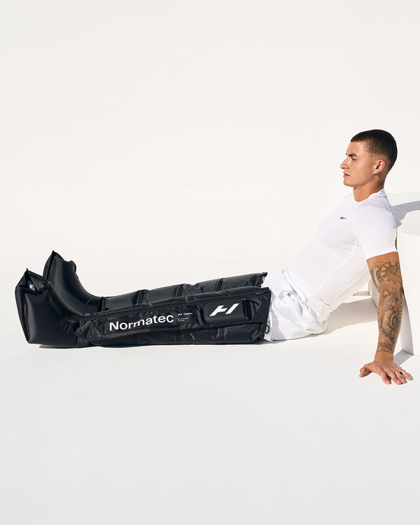 Person sitting on ground wearing a black Normatec compression device on a white background