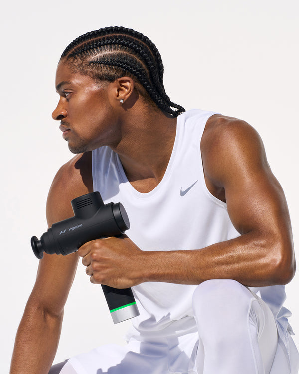 Person crouched, holding a massage gun in their hand with a white background