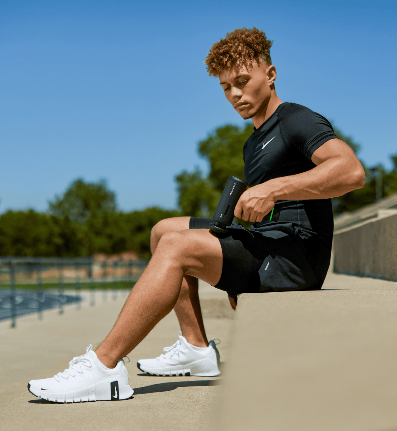 Person in athletic wear sitting outdoors with a clear blue sky using a hypervolt go 3 on their leg