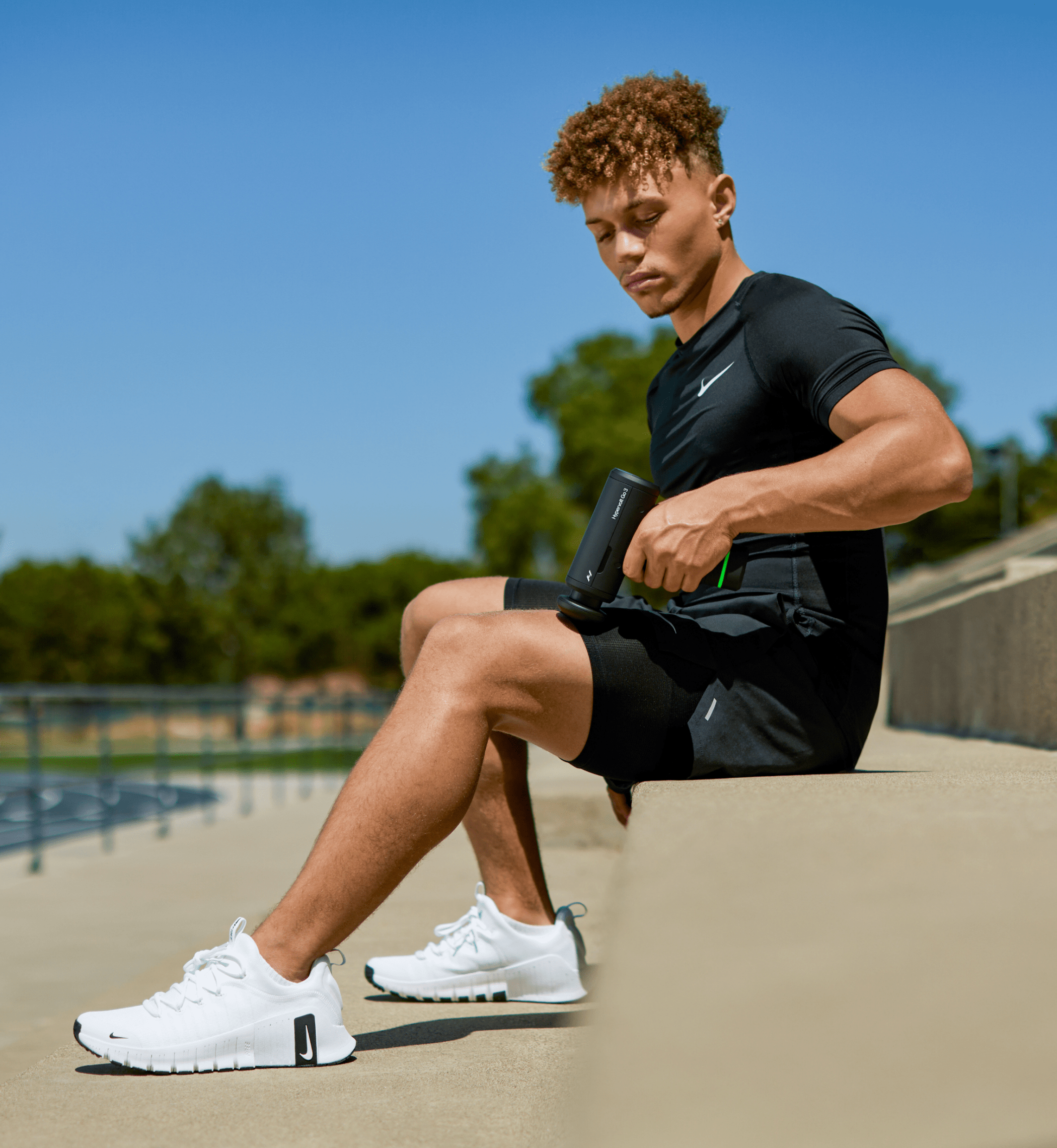 Person in athletic wear sitting outdoors with a clear blue sky using a hypervolt go 3 on their leg
