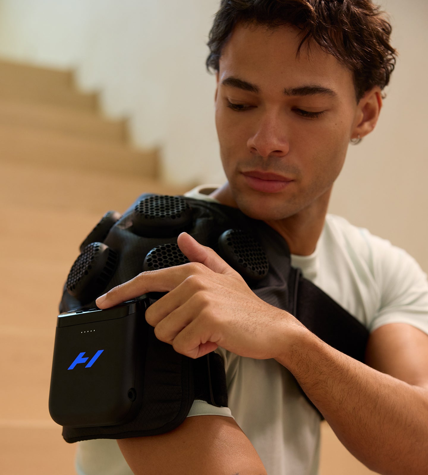Person using the Hyperice X 2 Shoulder on their right shoulder sitting on an indoor staircase