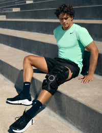 Man sitting on steps wearing a green Nike shirt hyperice x 2 knee device.