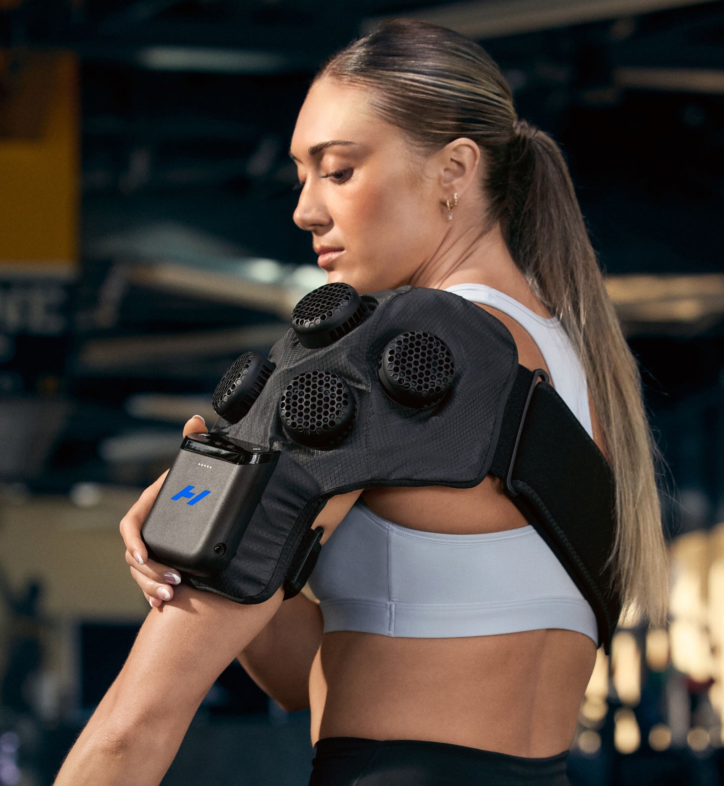 Woman wearing a Hyperice X 2 shoulder device with a blurred indoor background