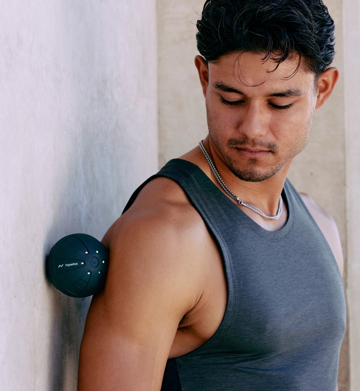 Man wearing a gray tank top pressing a hypersphere go between his shoulder and a light-colored wall.