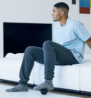 Man sitting on a white couch in a modern living room using a Hypersphere go on his foot.