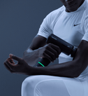 Person using a hypervolt 3 massage gun on their arm with a dark background