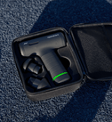 Hypervolt Go 3 massage device with green battery light in a black case on a textured blue surface