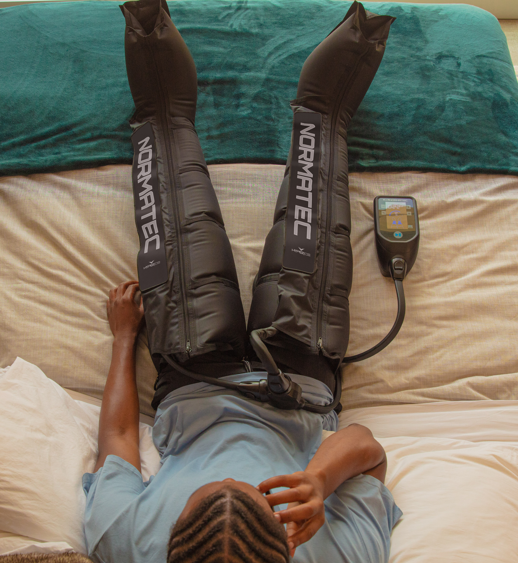 Person using Normatec compression devices on a bed
