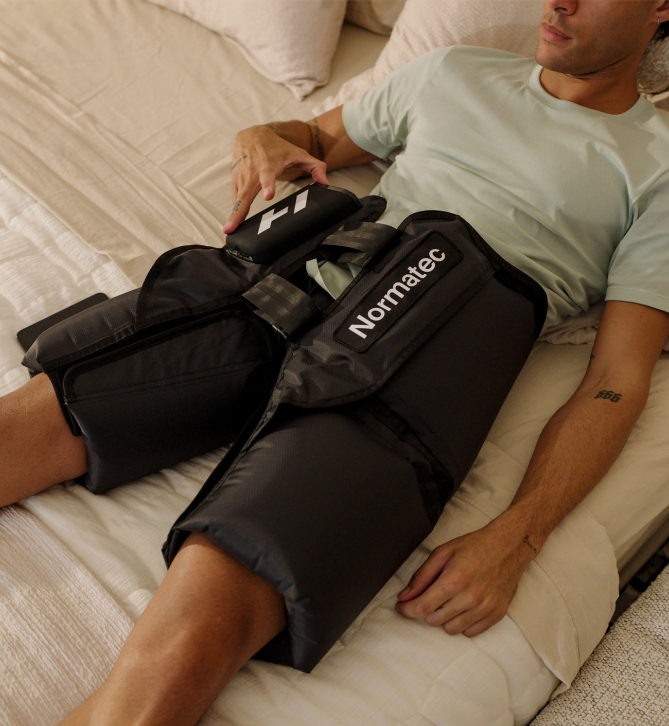 Persona usando un dispositivo de compresión Normatec elite hips en sus caderas en un dormitorio.