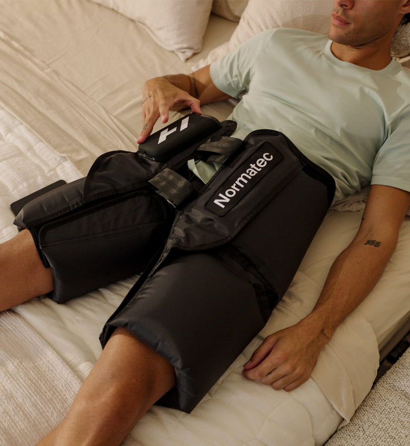 Person using a Normatec elite hips compression device on their hips in a bedroom setting.