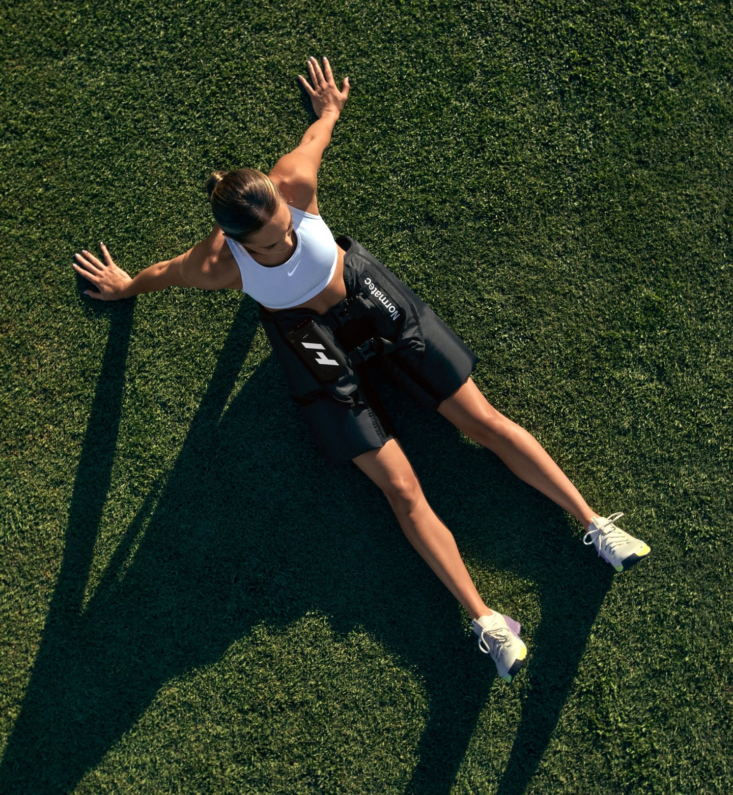 Una persona sentada en un campo de hierba con los brazos extendidos, usando Normatec Elite para caderas