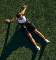 Una persona sentada en un campo de hierba con los brazos extendidos, usando Normatec Elite para caderas