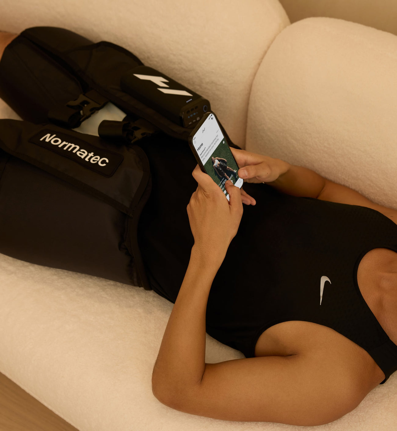 Persona acostada en un sofá usando un teléfono inteligente con Normatec elite en las caderas
