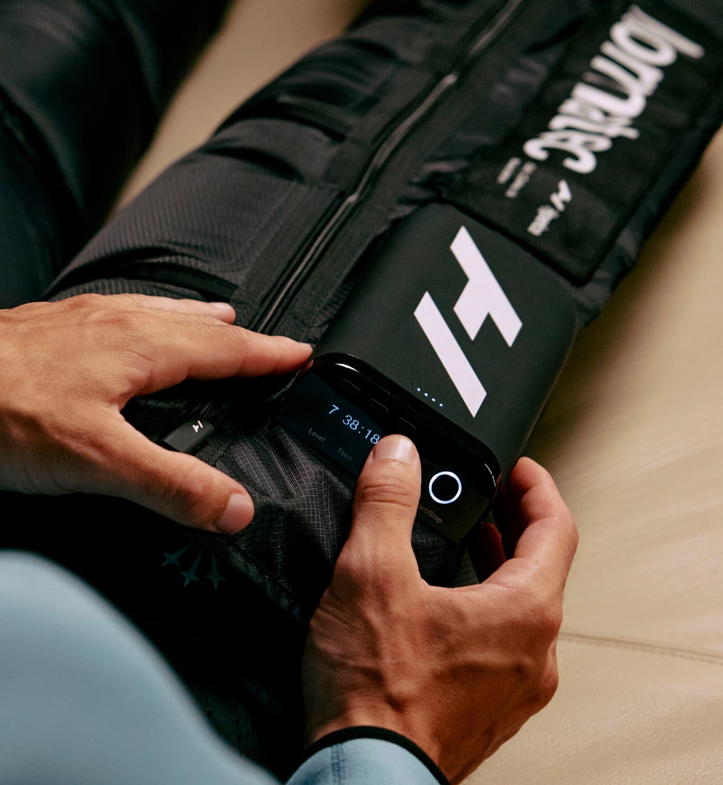 person sitting on a couch adjusting the control unit on their normatec elite leg unit