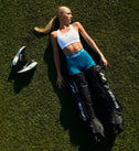 Mujer con ropa deportiva acostada sobre el césped junto a las Hyperboot Nike x Hyperice, usando las piernas Normatec elite