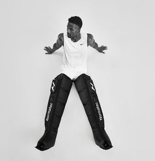 Person sitting on ground wearing Normatec elite legs on a white background