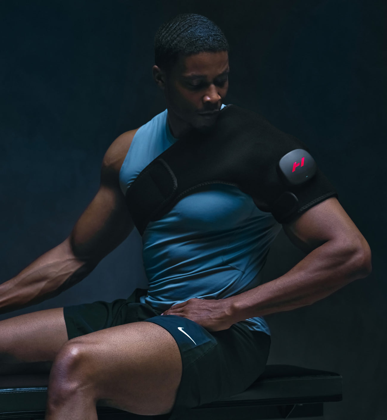 Personne portant une tenue de sport noire et bleue avec un sac à dos Venom 2, assise devant un fond sombre.