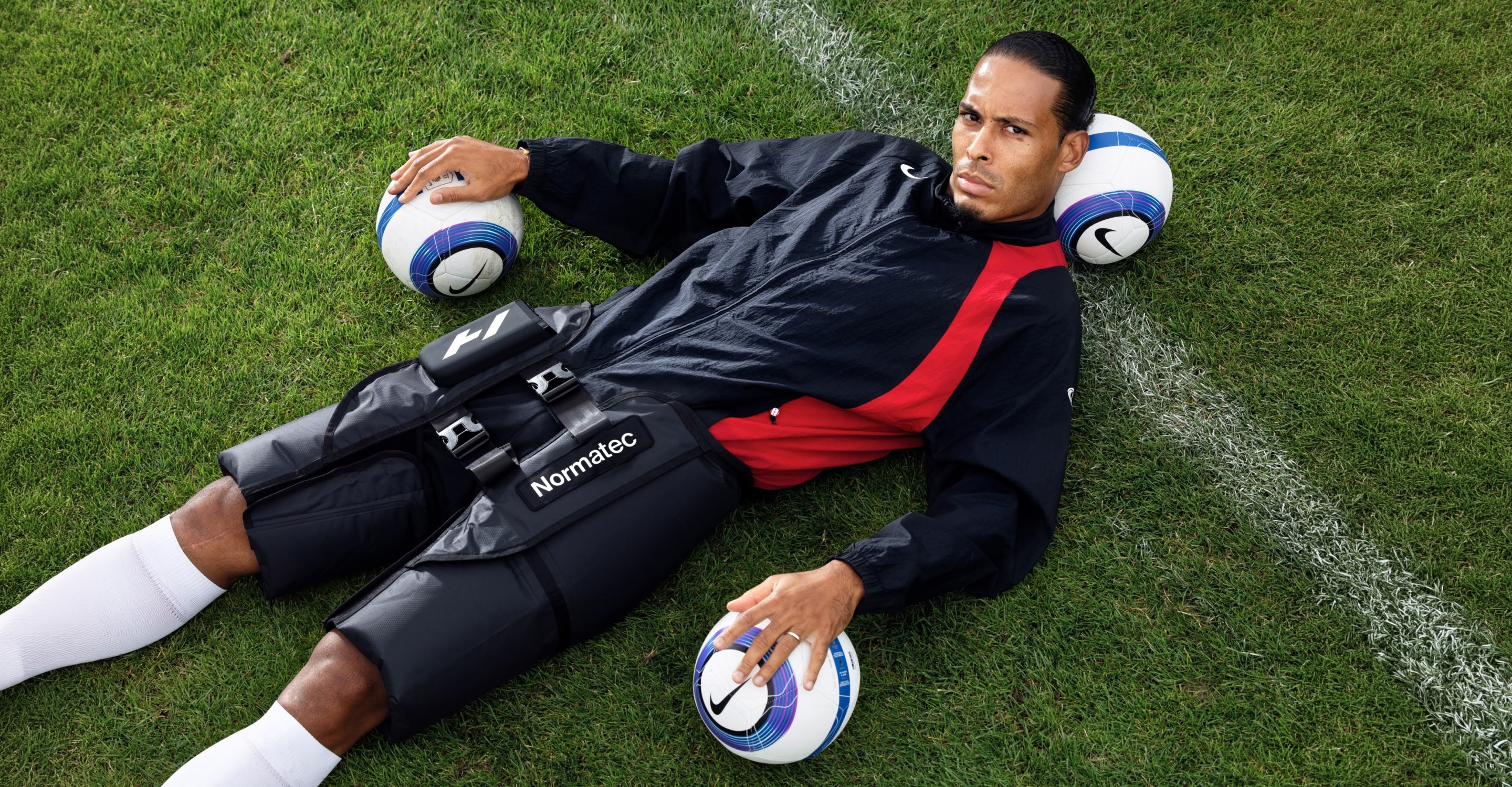 virgil van dijk lying on a soccer field with soccer balls and wearing normatec elite hips